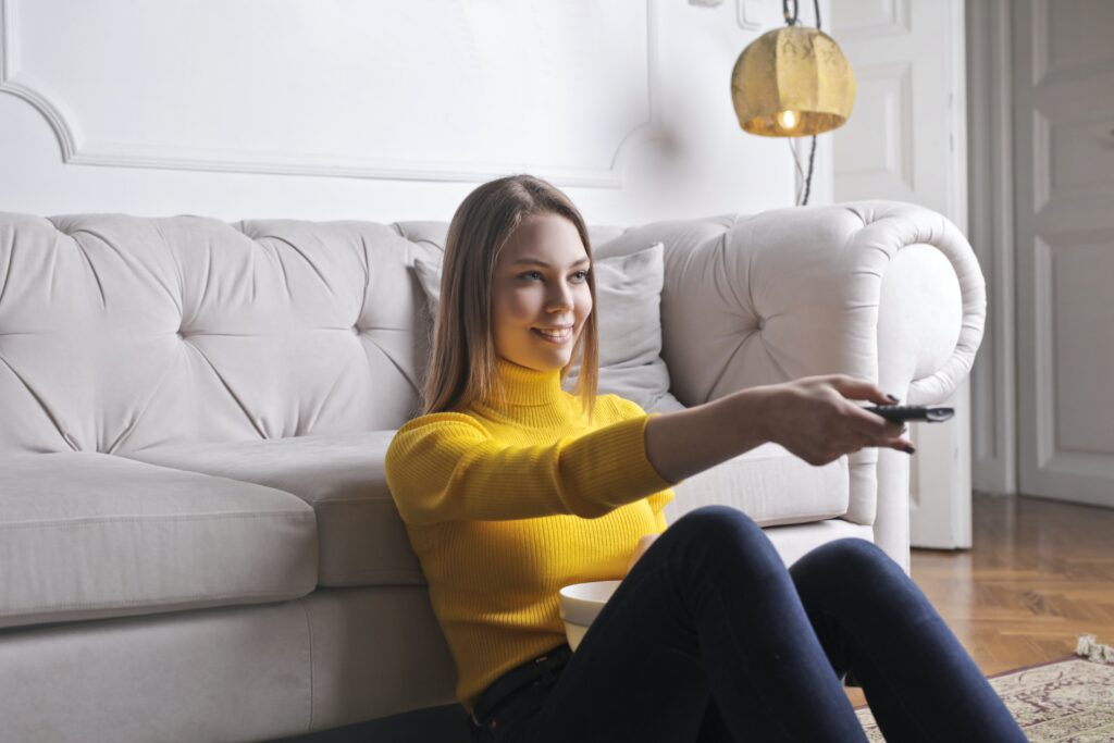 Young Woman Sitting On Floor Looking Happy With TV Remote. Feel Better