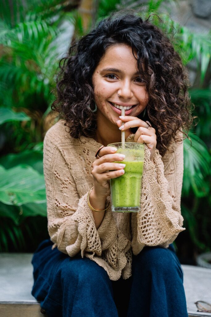 Young Woman Drinking A Green Smoothie Through A Straw