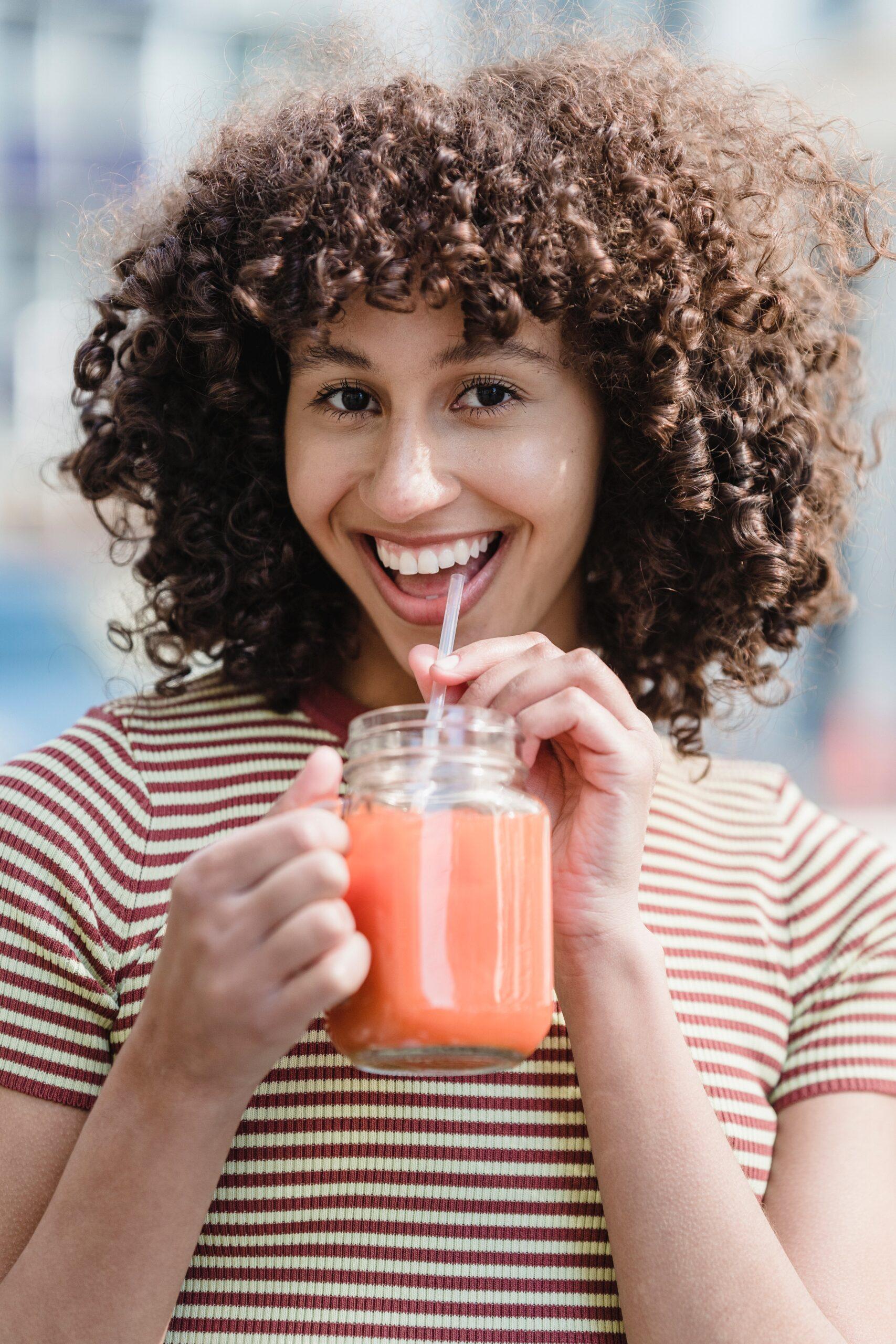 Young Woman Smiling Whilst Drinking A Smoothie Through A Straw